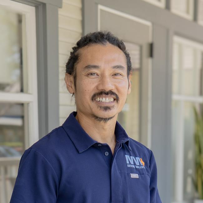 A photo of Dr. Cao smiling to the camera, wearing FIGS navy blue scrubs with the IVVH logo